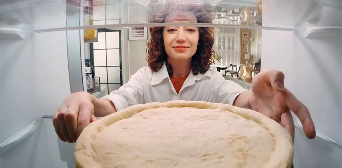View from inside the refrigerator of a woman loading a pizza dough